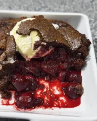 A slice of chocolate cherry dump cake with a scoop of vanilla ice cream on a white plate