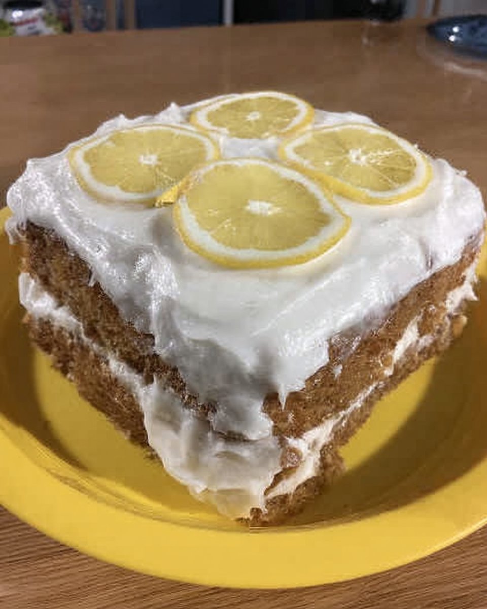 Whole frosted lemon cake on a ceramic cake stand