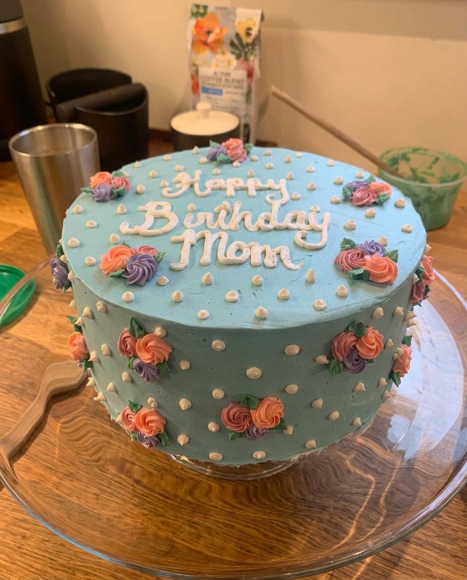 A close up of a hand using a small spatula to paint a flower on a cake
