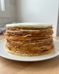 A tall stack of thin crepes layered with chocolate cream and topped with glossy ganache
