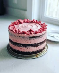 A sliced strawberry chocolate cake with white frosting and fresh berries