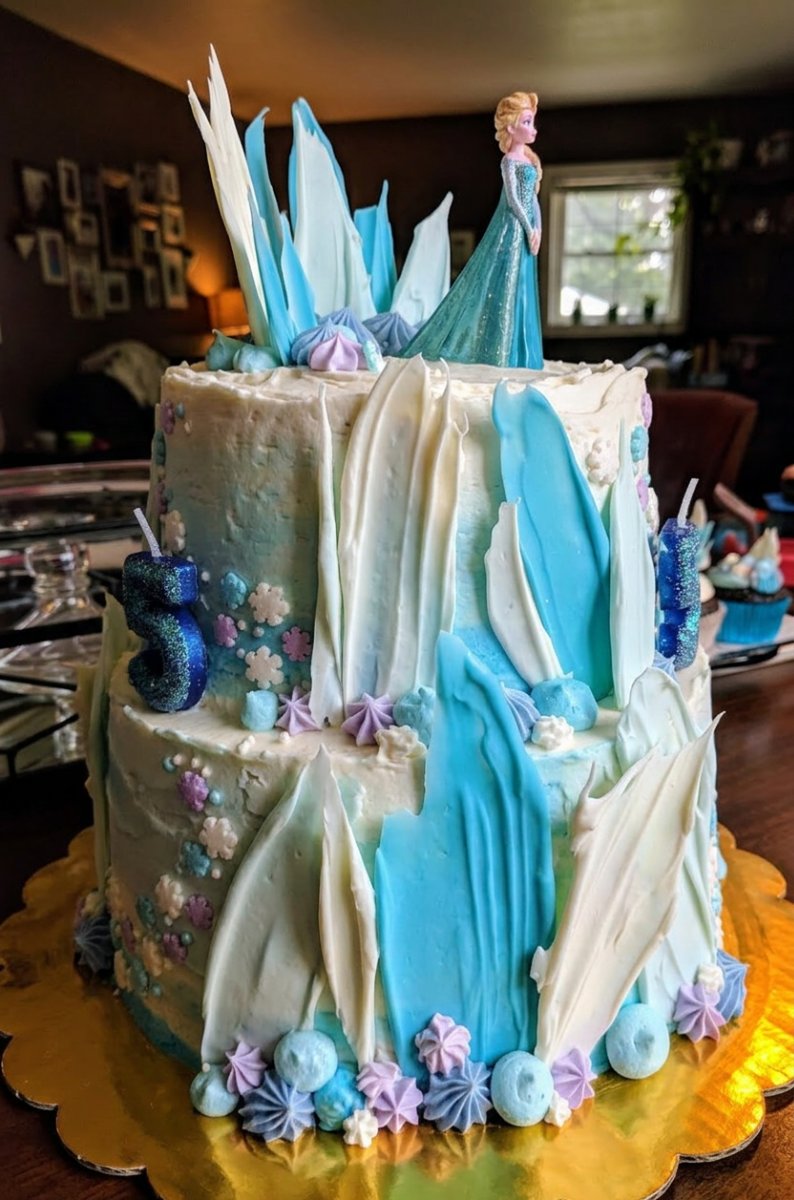 A beautiful Frozen Cake featuring fondant Elsa and Olaf figures with a blue sugar castle.