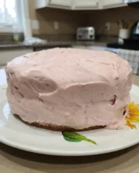 A beautiful fresh strawberry cake with pink frosting on a white cake stand