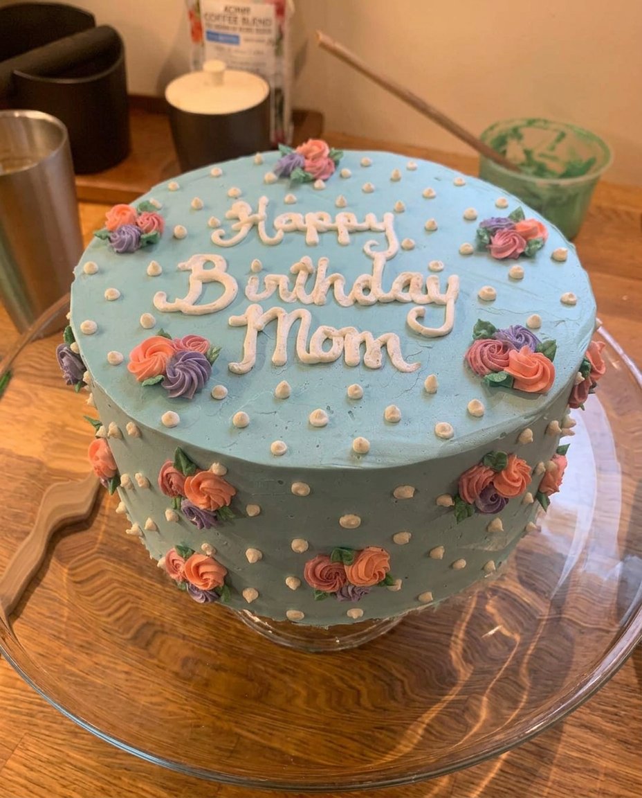 A white birthday cake decorated with spatula-painted white flowers and green leaves