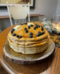 A hyperrealistic cake that looks like a tall stack of pancakes with syrup and blueberries