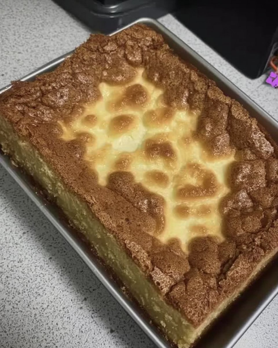 A square slice of ooey gooey butter cake on a white plate with powdered sugar