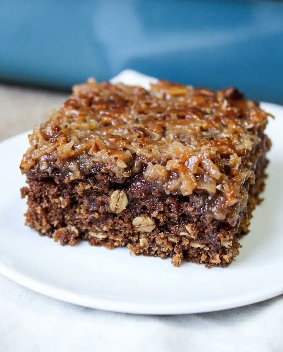 A slice of oatmeal cake on a white plate served with a cup of coffee and a spoon