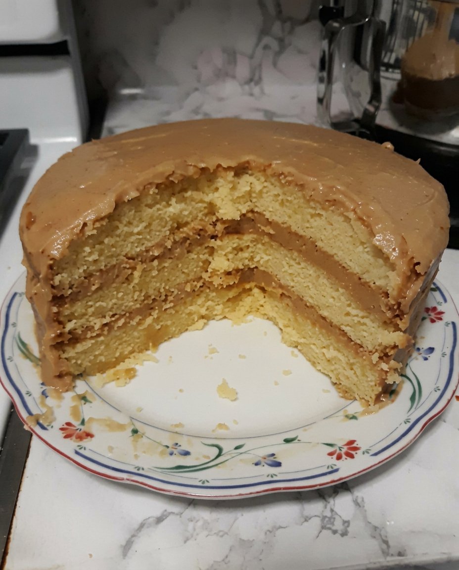 A single slice of caramel cake on a white plate showing the moist interior and thick frosting.