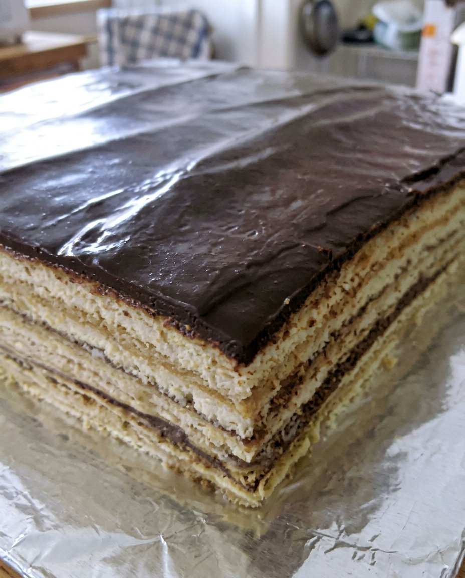A rectangular slice of Opera Cake served on a decorative gold plate with a fork