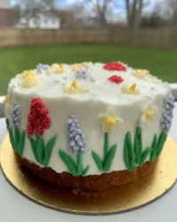 A tall Spring Cake decorated with buttercream flowers and birch bark frosting on a white stand