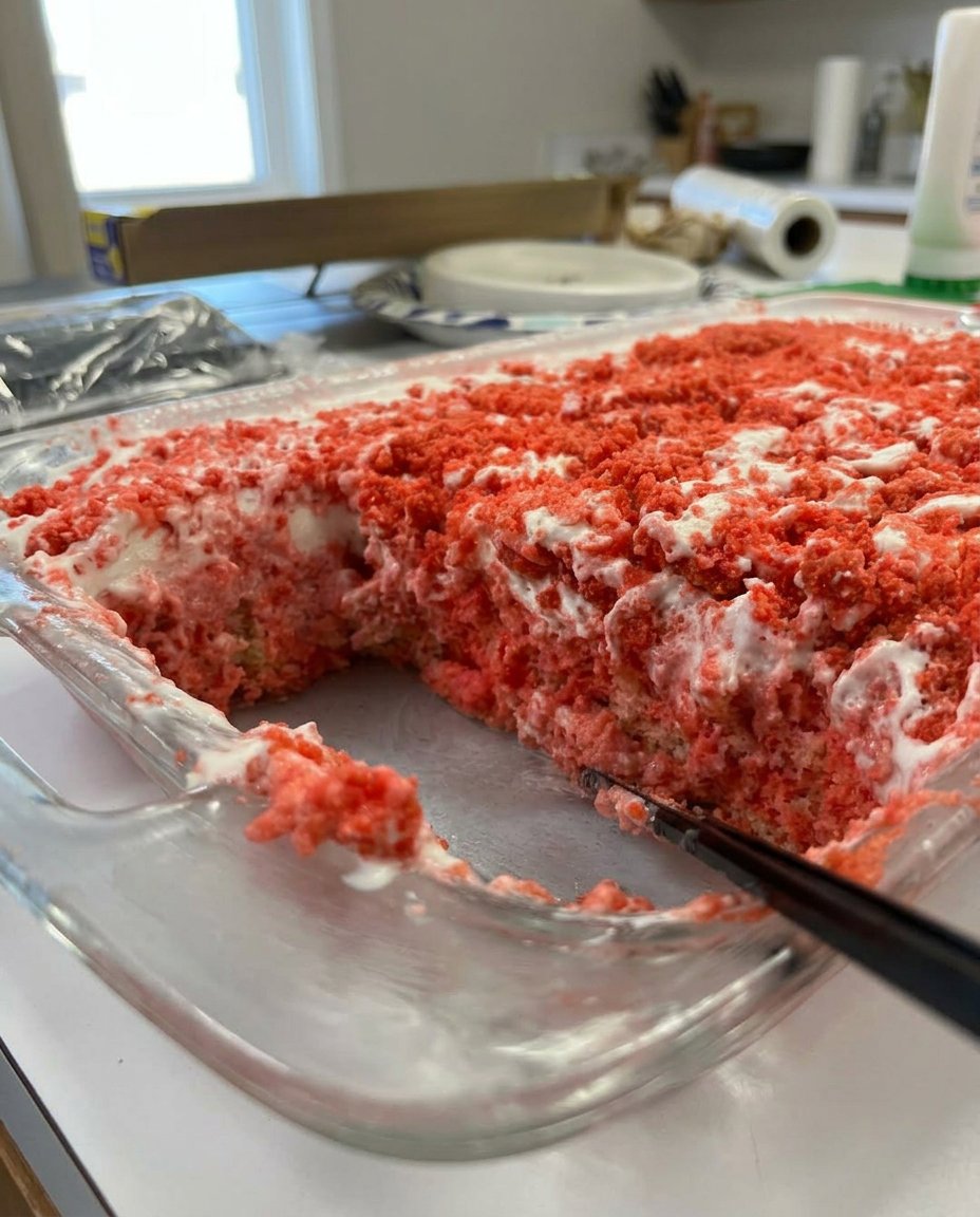 A close up shot of a slice of strawberry crunch cake with pink gelatin layers and a golden oreo topping