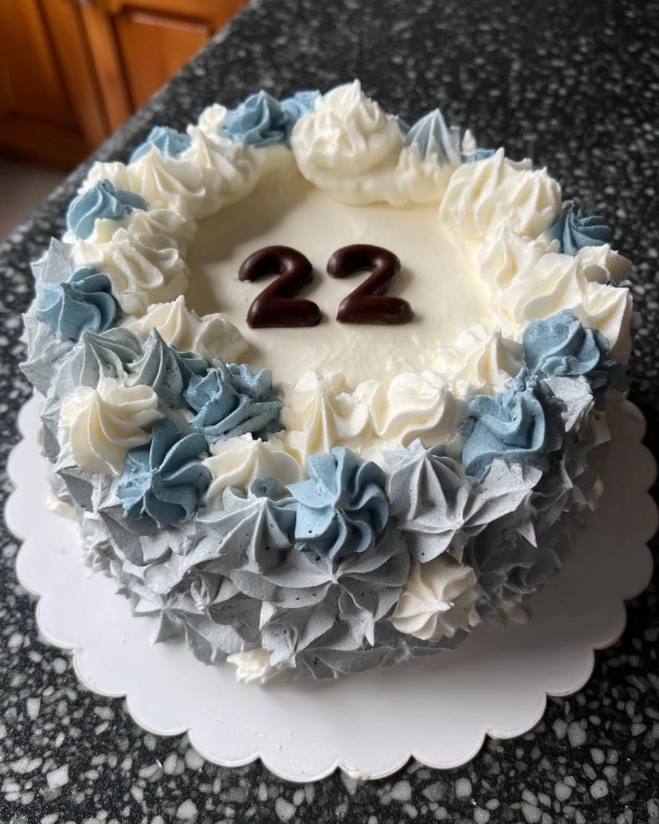A tall ombre cake with a blue and green gradient frosting decorated with blueberries and flowers