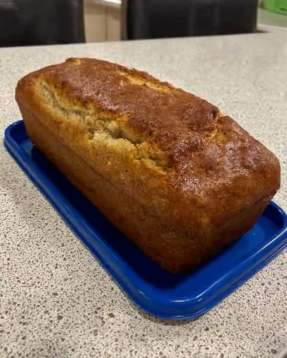 A hand whisking smooth yellow lemon cake batter in a glass bowl