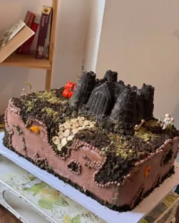 A large tiered yellow cake decorated like a castle with pink cone turrets and green vines.