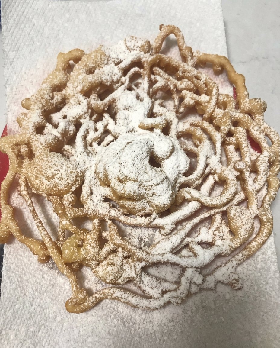 A golden brown homemade funnel cake dusted with powdered sugar on a simple plate
