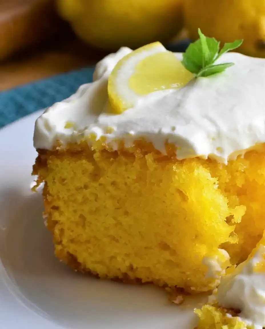 A slice of lemon poke cake served on a casual plate with berries and whipped cream