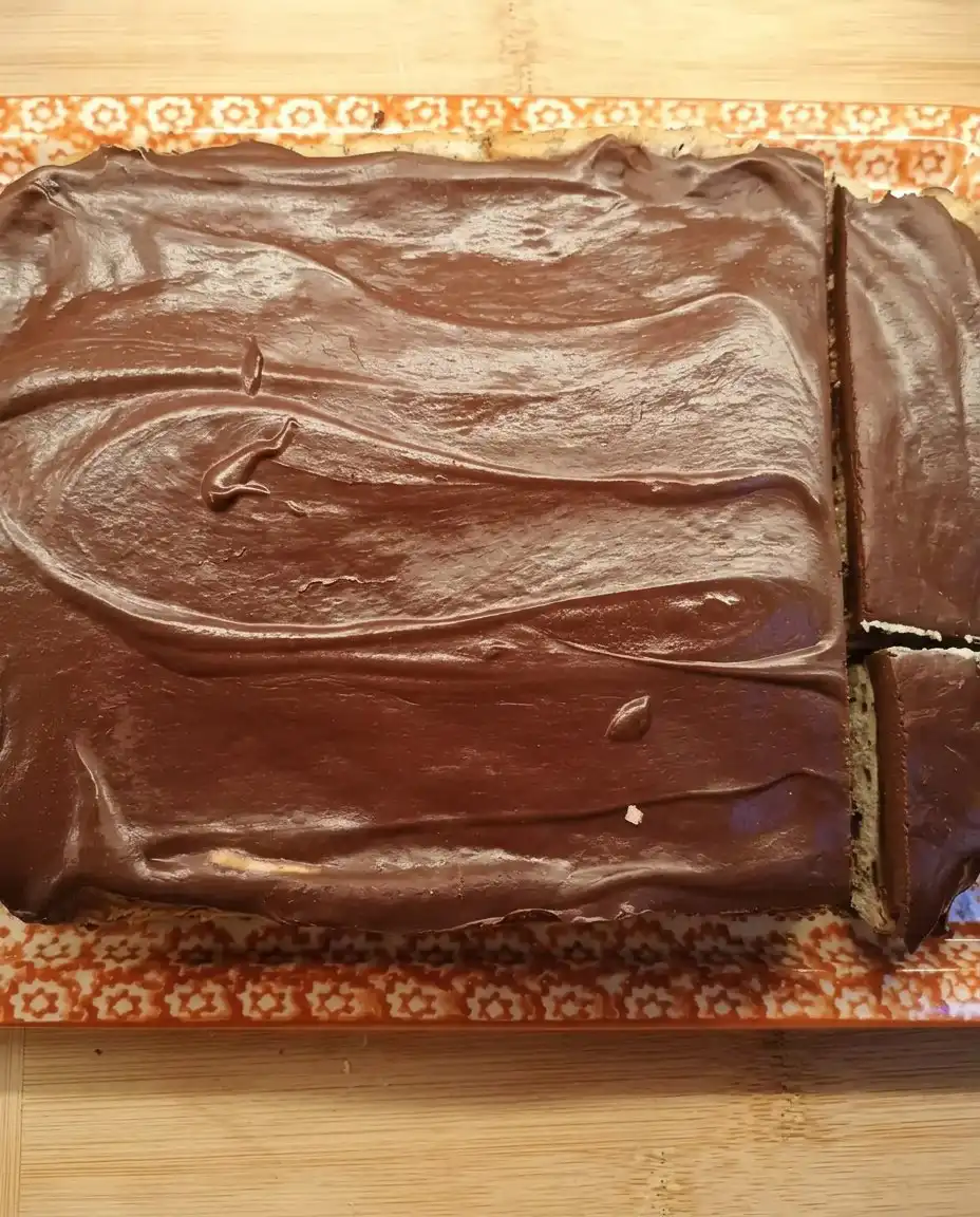 A slice of chocolate ganache cake on a small plate next to a glass of milk