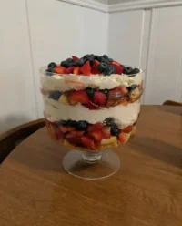 A large glass trifle bowl filled with distinct layers of angel food cake, white chocolate pudding, strawberries, and blueberries