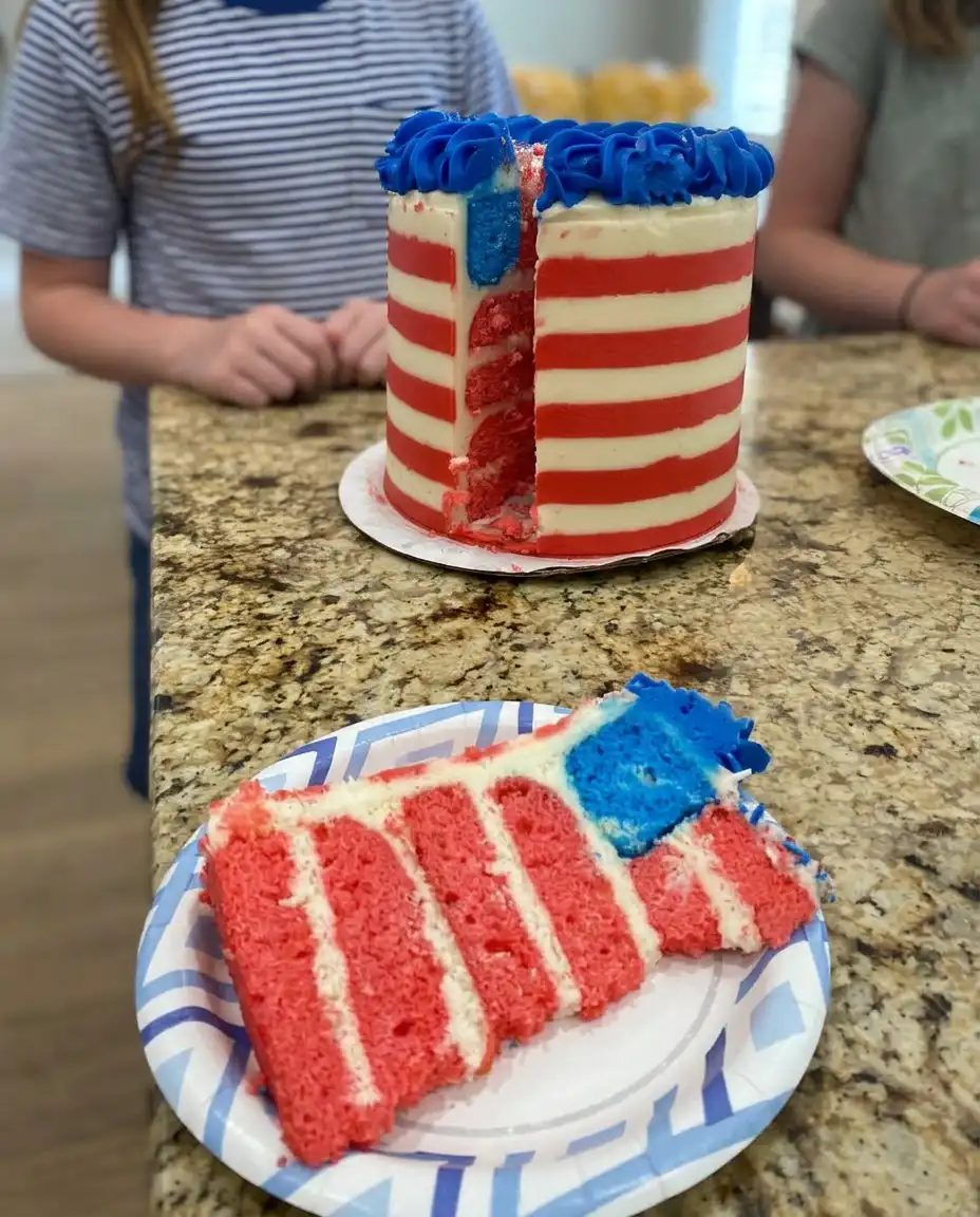 A slice of American flag cake on a white plate with a fork.