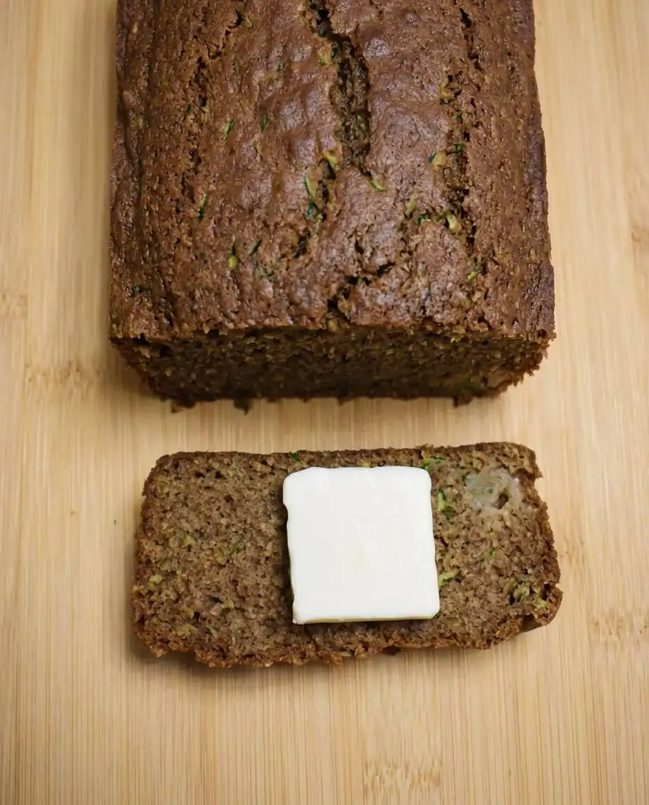 A thick slice of apple zucchini bread served with a pat of butter.