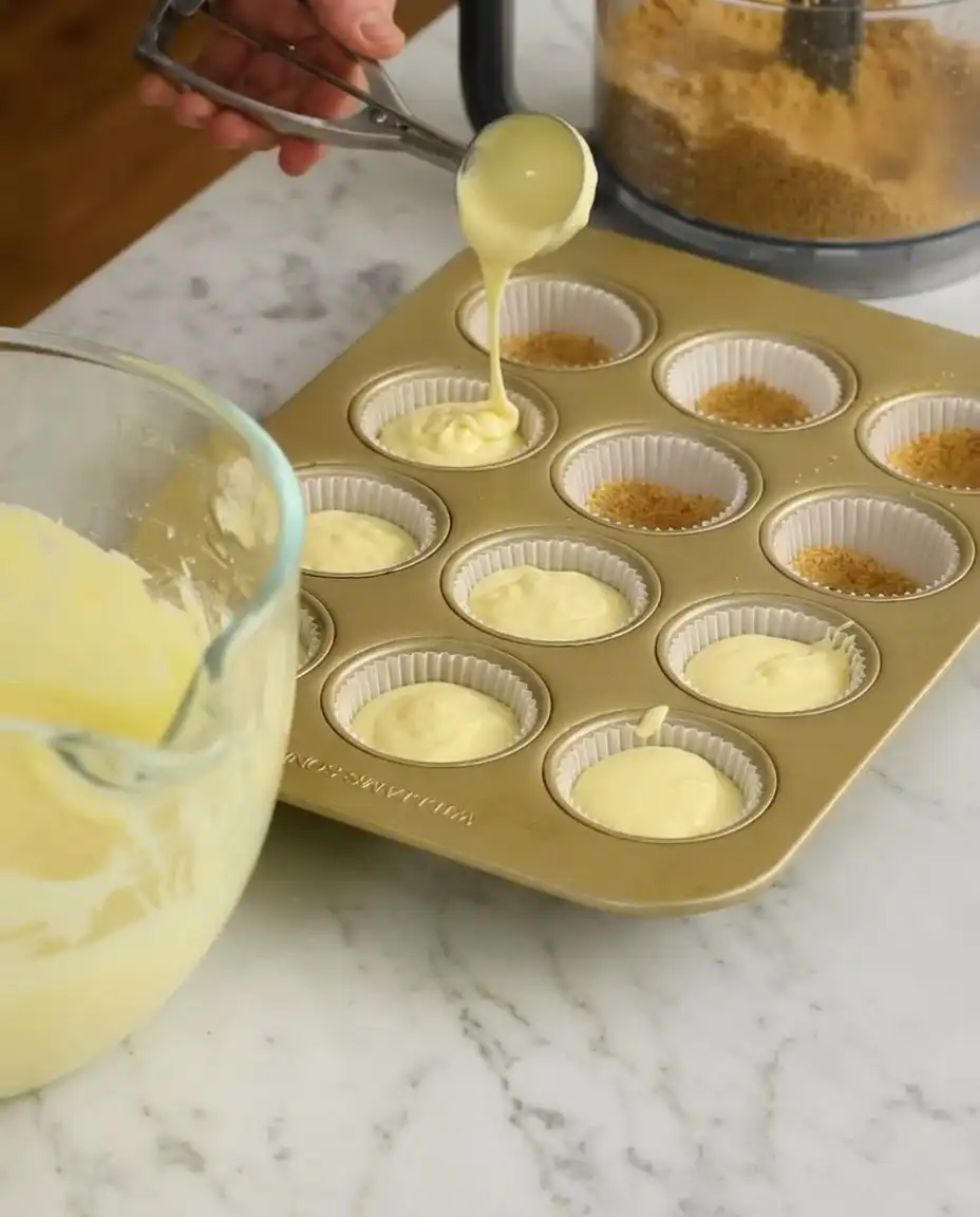Close up of smooth cheesecake batter being scooped into muffin liners.