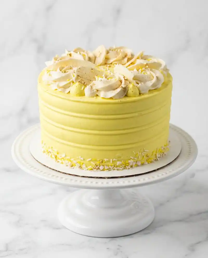 A tall banana pudding layer cake with yellow frosting and vanilla wafers on top.