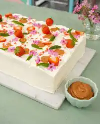 A close up of the Best Strawberry Sheet Cake decorated with fresh mint and edible flowers.