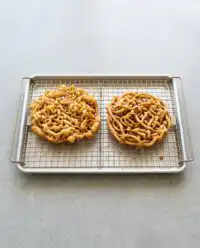 A golden brown Classic Carnival Funnel Cake heavily dusted with white powdered sugar on a plate.