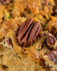 A golden brown loaf of carrot apple zucchini bread on a wooden board