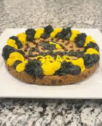 A thick chewy cookie cake with colorful buttercream frosting and chocolate chips