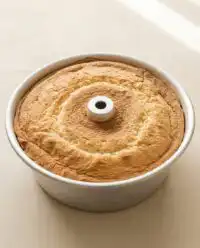 A golden brown Classic Peach Pound Cake resting on a cooling rack with fruit on top.