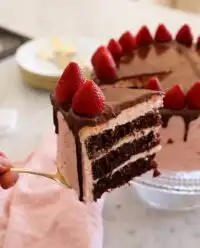 A three layer chocolate strawberry cake with dark ganache dripping down the sides and fresh berries on top.