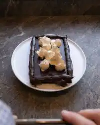 A tall slice of Peanut Butter Fudge Cake showing three layers of chocolate cake and peanut butter frosting