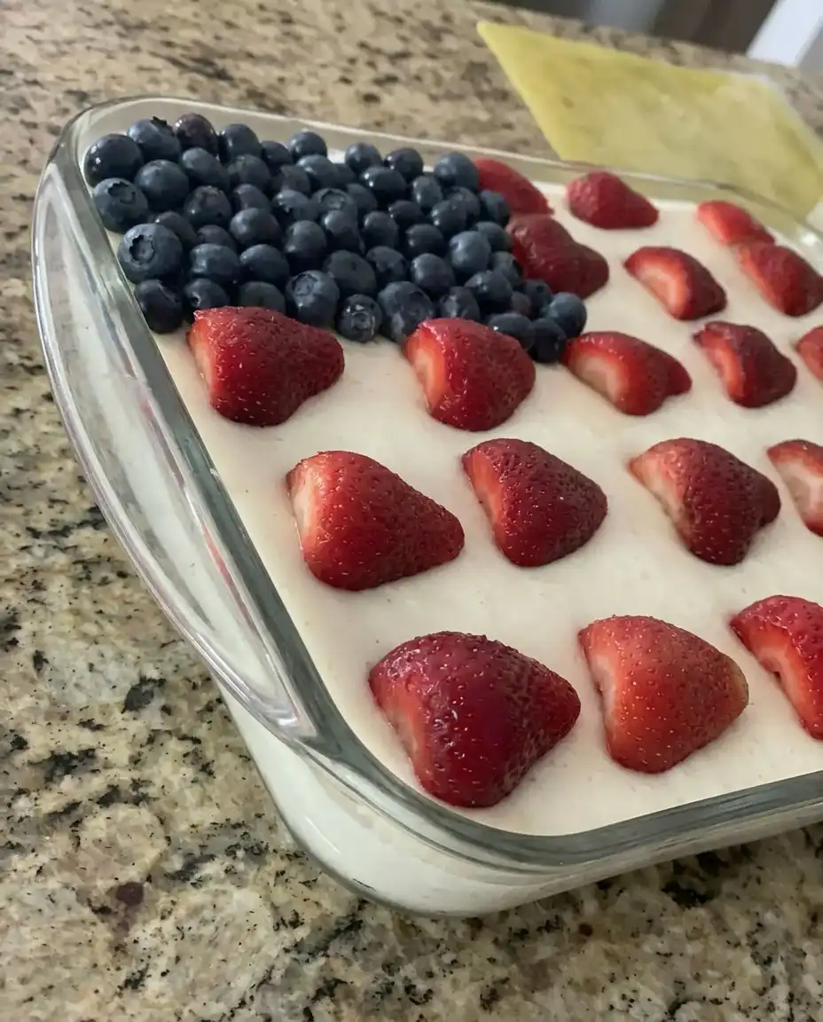 Hand arranging strawberry slices as stripes on a white cake