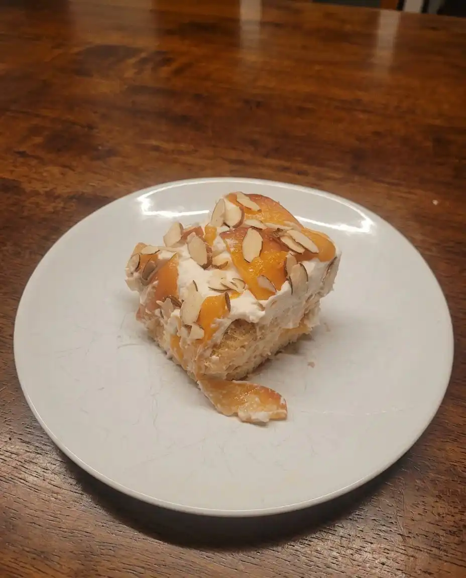 A hand dipping a ladyfinger cookie into a shallow bowl of peach syrup