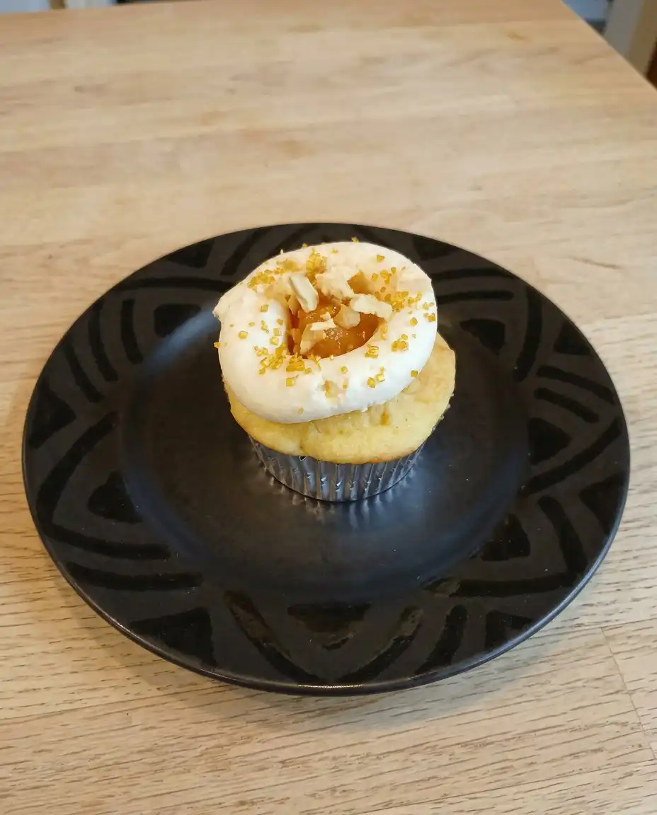 A close up of a single peach honey cheesecake cupcake with a bite taken out.