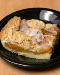 A golden brown Peach Coffee Cake topped with nutmeg and a sweet glaze sitting in a glass dish.