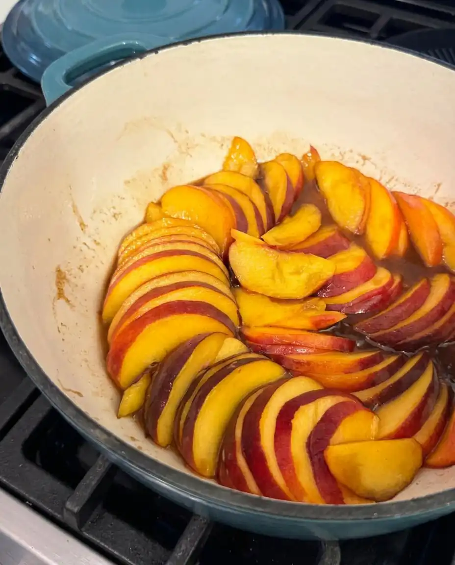 Sliced fresh peaches next to flour, sugar, and butter on a wooden counter.