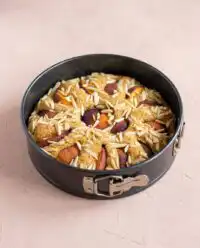A golden Sour Cream Peach Coffee Cake cooling on a wire rack with fresh peach slices nearby.