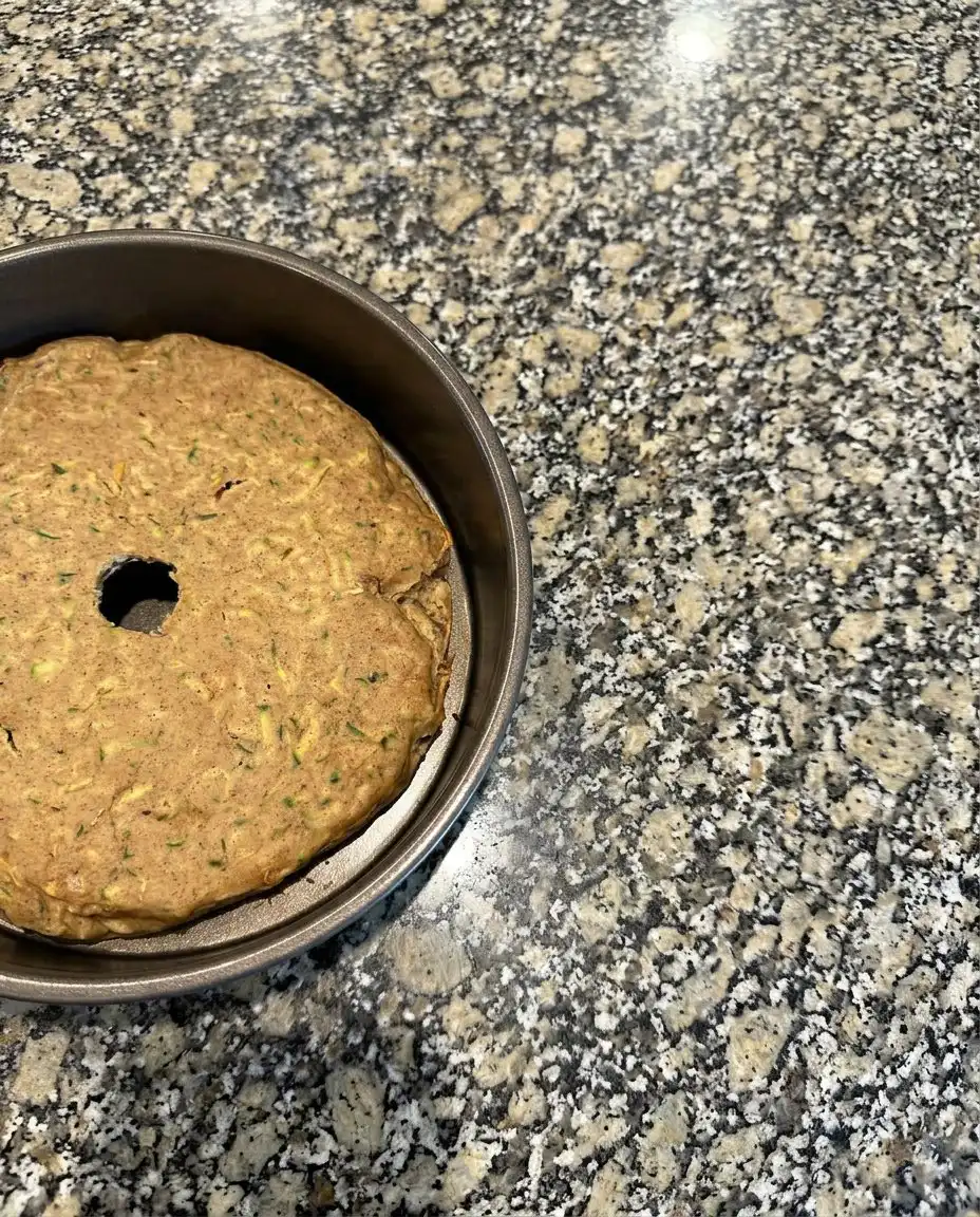 Hands grating a fresh zucchini into a glass bowl for baking.