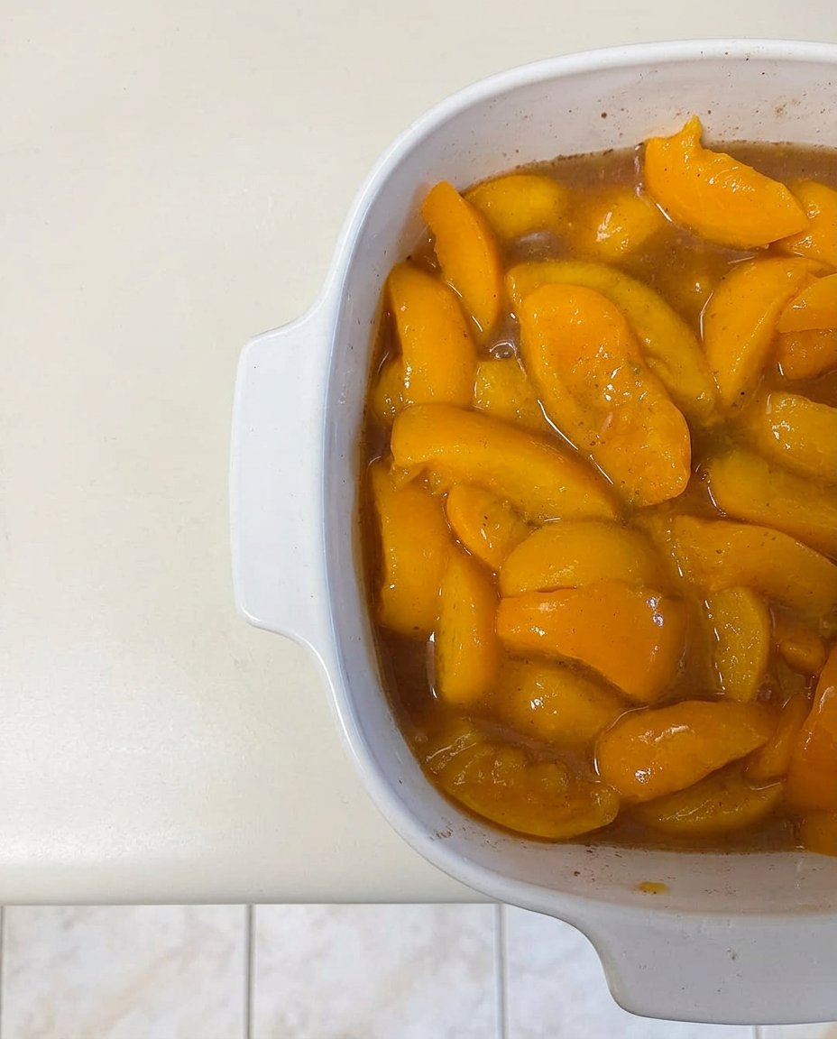 Cans of peach filling, a box of vanilla cake mix, and a stick of butter on a counter.