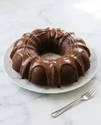 A close up shot of a fudgy slice of keto chocolate zucchini cake on a white ceramic plate