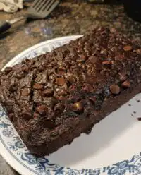 A fresh loaf of chocolate zucchini bread on a cooling rack with melted chocolate chips