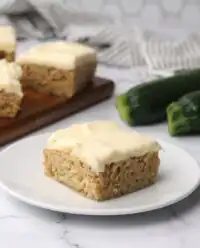 A close up view of frosted Zucchini Bars sitting on a wooden cutting board in a kitchen.
