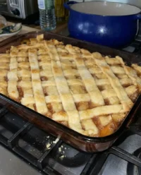 A golden brown old fashioned oven baked peach cobbler in a ceramic baking dish.