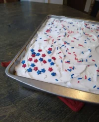 A festive red white and blue patriotic poke cake topped with whipped cream and sprinkles