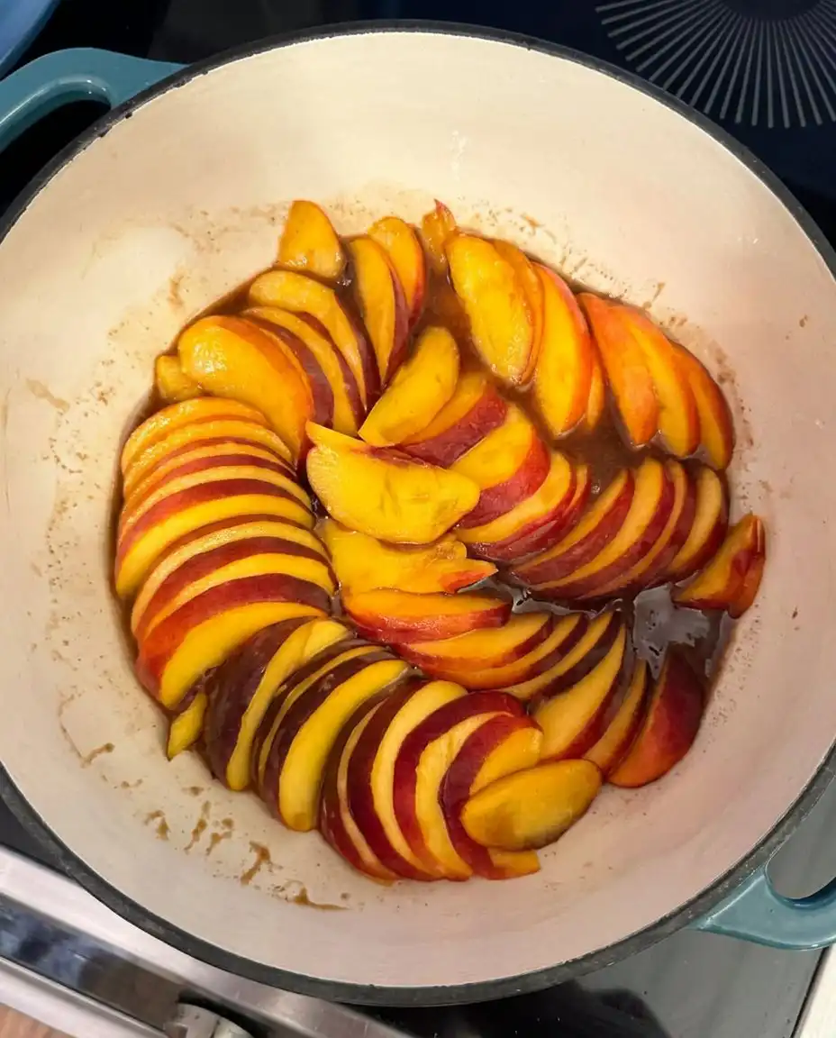Pouring golden bourbon caramel over sliced peaches in a cake pan