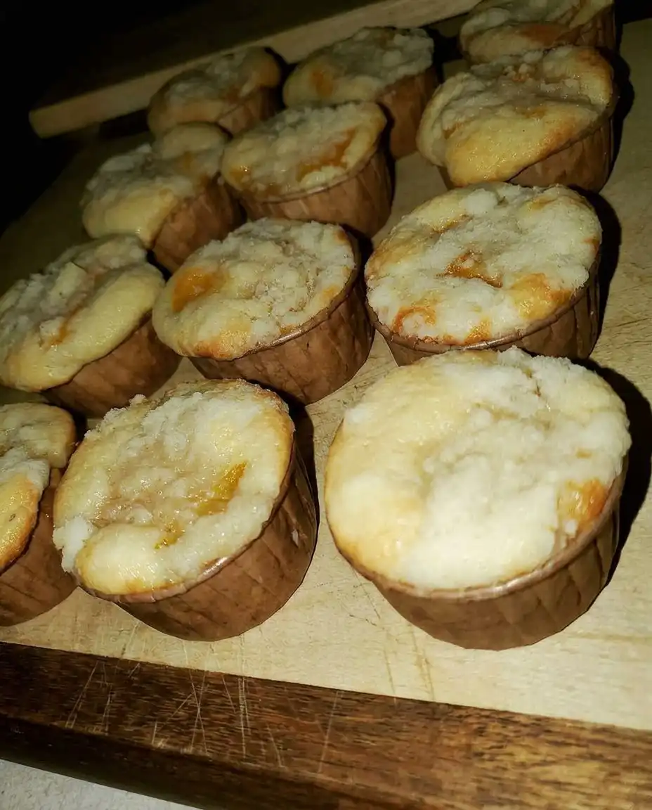 A peach cobbler muffin on a plate next to a cup of coffee