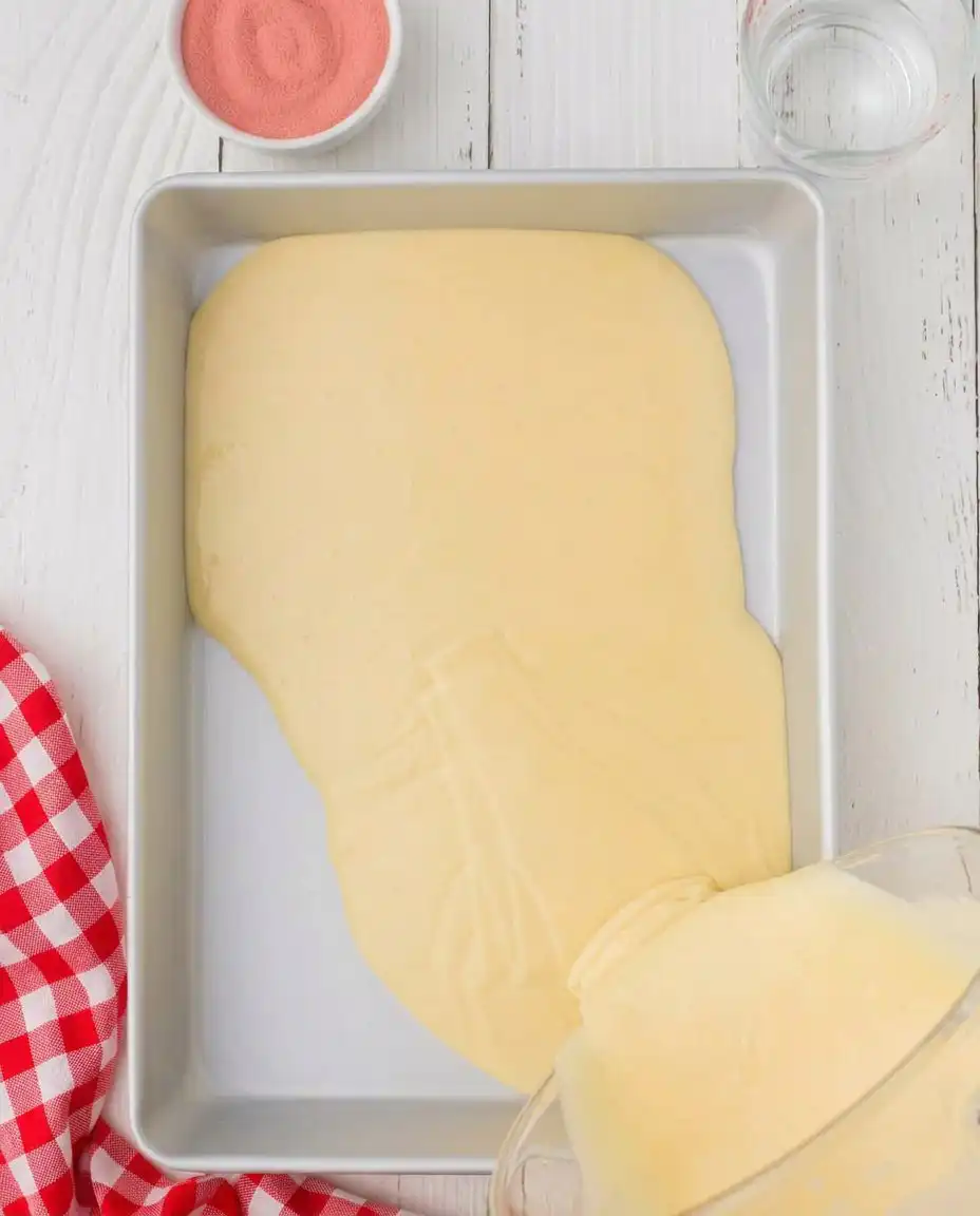 A fork poking holes into a baked vanilla cake in a glass pan