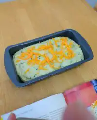 A golden brown loaf of Green Onion Zucchini Cheddar Quick Bread on a wooden board